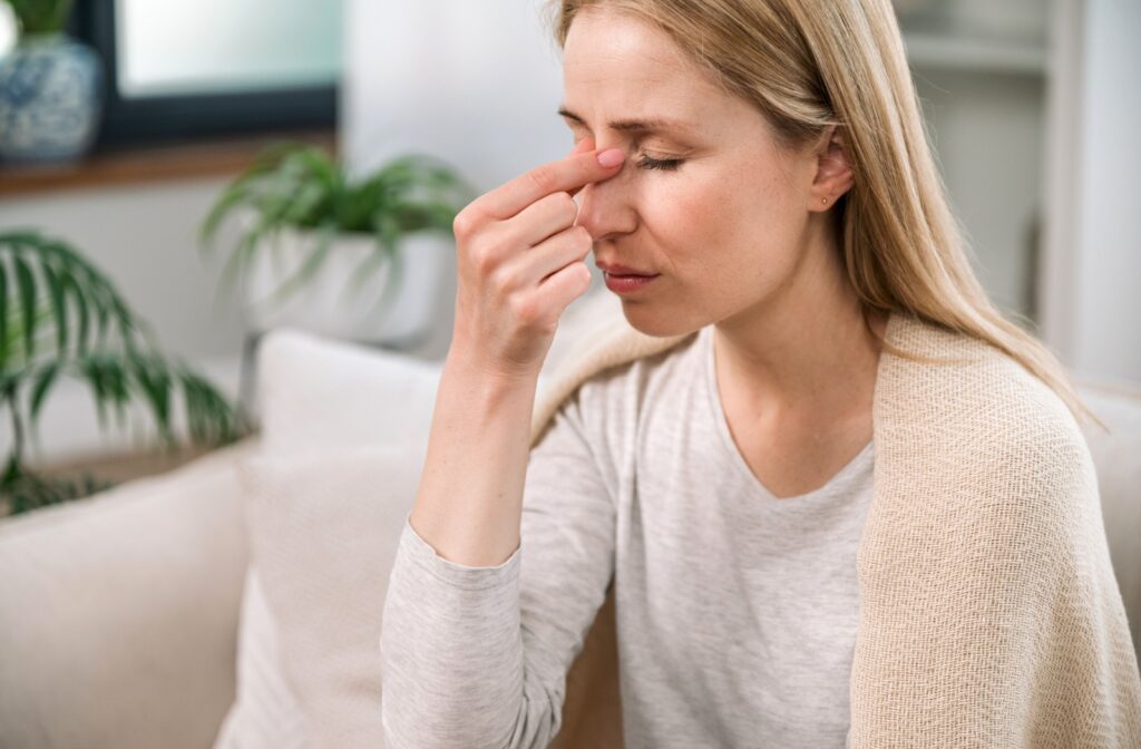 A young adult rubbing the bridge of their nose in frustration to find relief from their sinus infection while sitting at home.