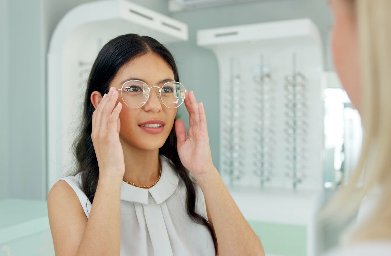 A woman looking in the mirror as she holds a pair of glasses up to her faced