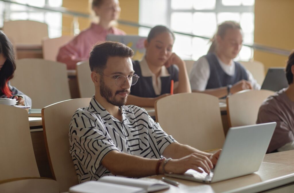 Person wearing glasses and sitting in a lecture hall typing on their laptop