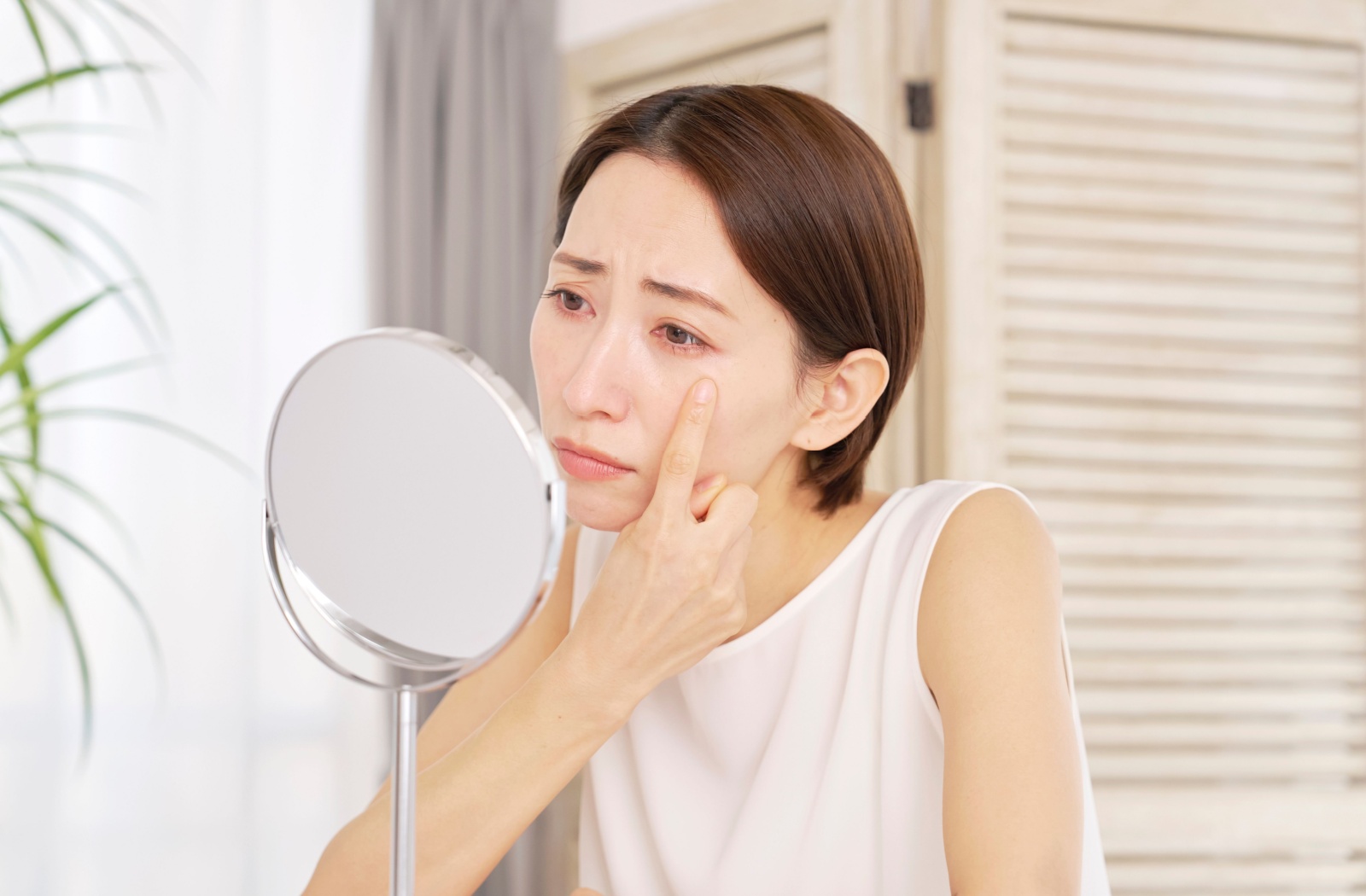 A person looks at their dry red eyes in the mirror