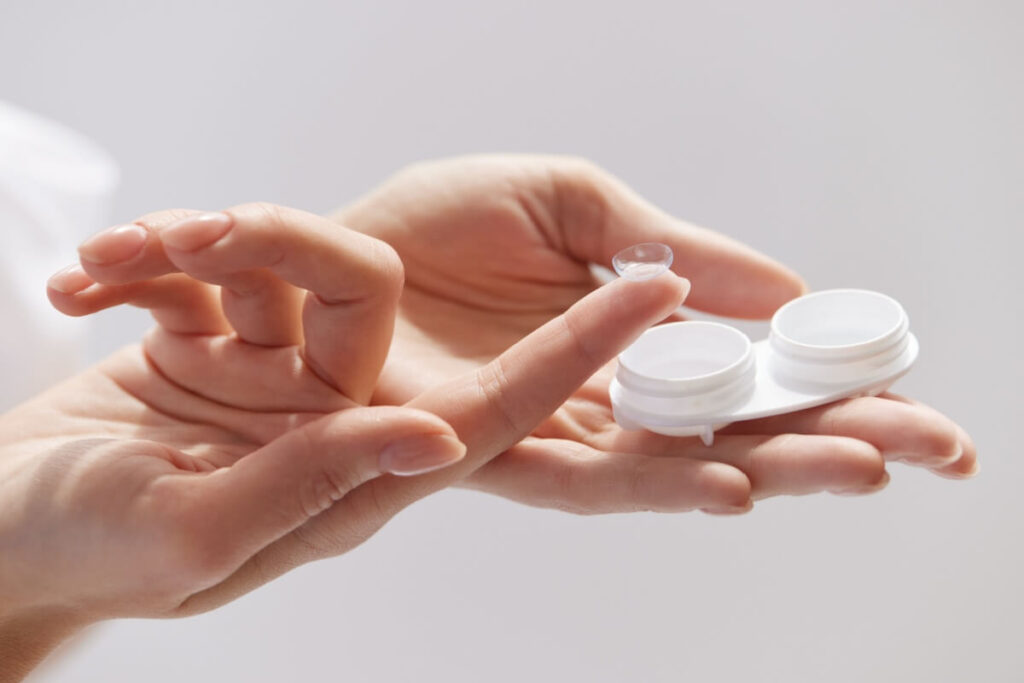 Close-up of a person holding a soft contact lens on their fingertip beside an open contact lens case, preparing to insert the lens.